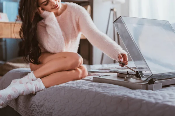 Selective focus of girl sitting on bed and turning on vinyl audio player at home — Stock Photo