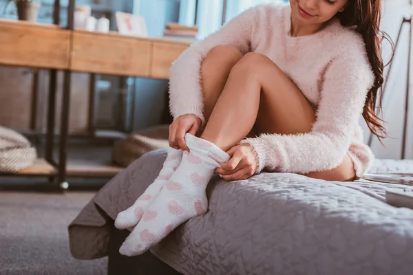 Partial view of girl putting on fluffy socks while sitting on bed at home — Stock Photo