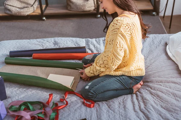 Частичный вид девушки упаковки рождественский подарок, сидя на кровати дома — стоковое фото