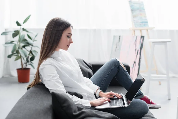 Selective focus of girl sitting on couch and using laptop in living room — Stock Photo