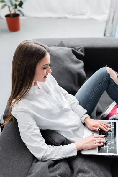 Привлекательная девушка сидит на диване и с помощью ноутбука в гостиной — стоковое фото