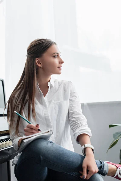 Hermosa chica en camisa blanca sentado y escribiendo en el cuaderno en casa - foto de stock