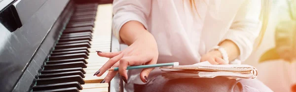 Ausgeschnittene Ansicht eines Mädchens mit Notizbuch, das zu Hause mit Hintergrundbeleuchtung Klavier spielt und Musik komponiert — Stockfoto