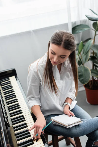 Привлекательная девушка с ноутбуком, играющая на пианино и сочиняющая музыку дома — стоковое фото
