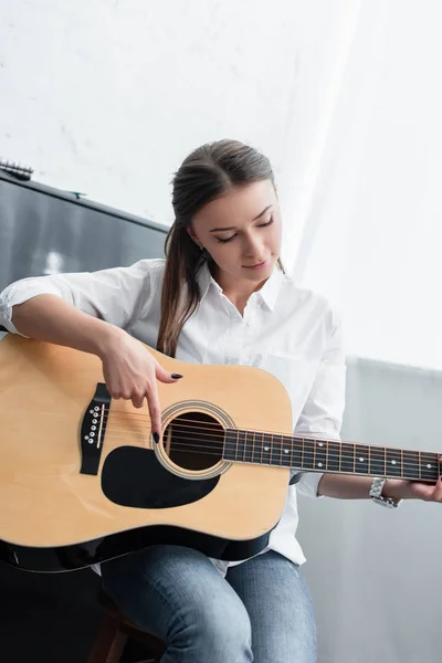 Hermosa chica sentada y tocando la guitarra en la sala de estar - foto de stock