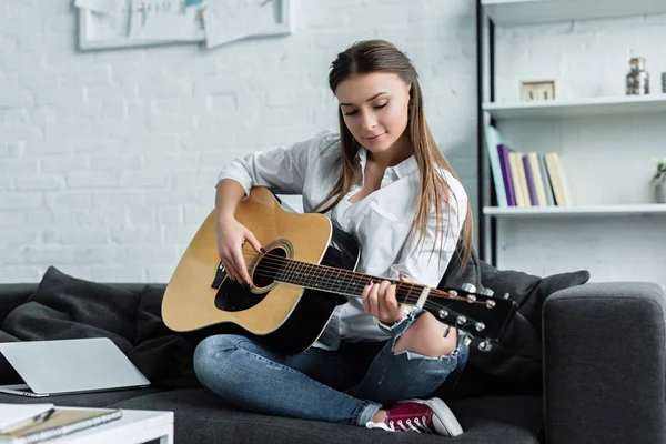 Konzentriertes Mädchen, das auf der Couch sitzt und im Wohnzimmer Gitarre spielt — Stockfoto