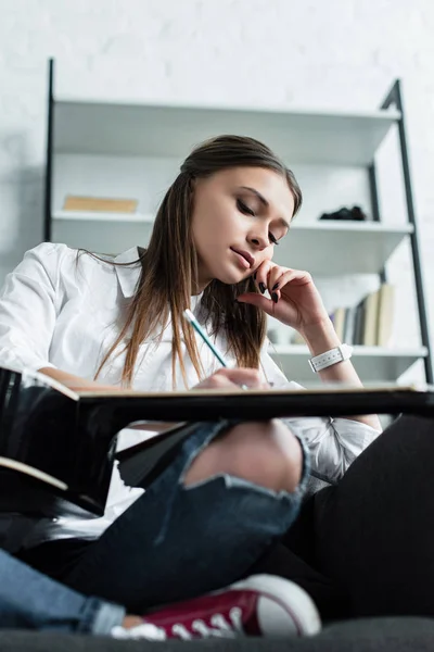 Schöne nachdenkliche Mädchen sitzt mit Gitarre und komponiert Musik zu Hause — Stockfoto