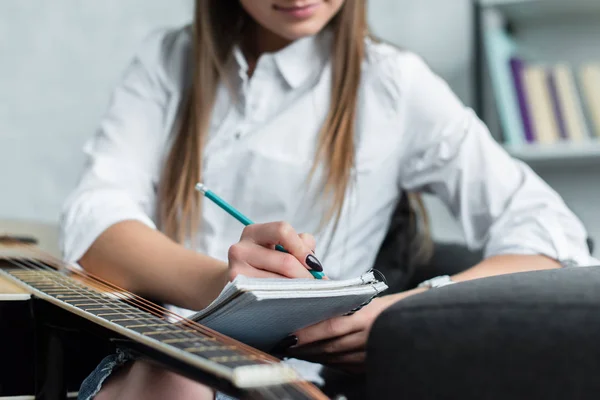 Ausgeschnittene Ansicht eines Mädchens, das mit Gitarre zu Hause sitzt und Musik komponiert — Stockfoto