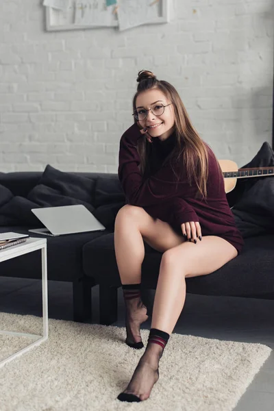 Красивая девушка смотрит на камеру и сидит на диване в гостиной — стоковое фото