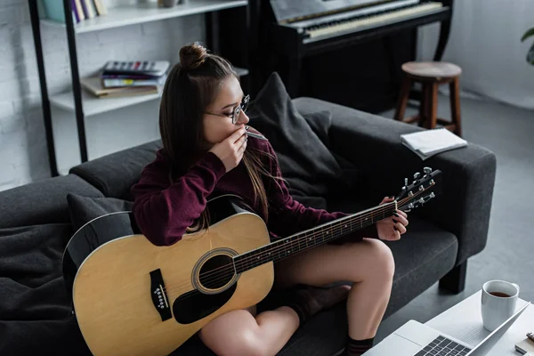 Chica sentada en el sofá con la guitarra y fumar marihuana conjunta en la sala de estar - foto de stock