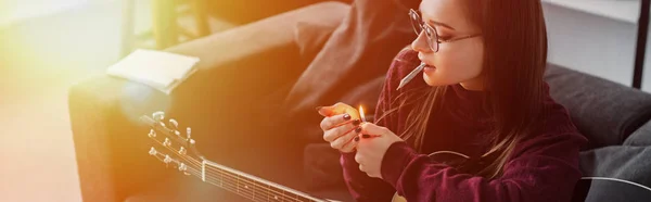 Fille allumant joint de marijuana et tenant guitare à la maison avec rétro-éclairé et copier l'espace — Photo de stock