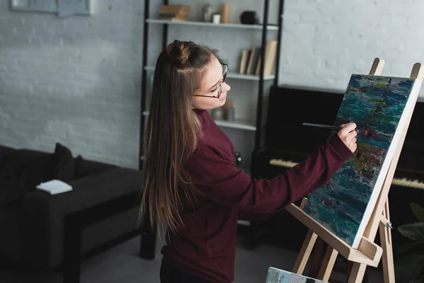 Beautiful girl in burgundy sweater painting on canvas at home — Stock Photo