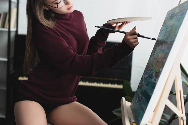 Обрезанный вид девушки в бордовом свитере сидя, держа палитру и живопись дома — стоковое фото