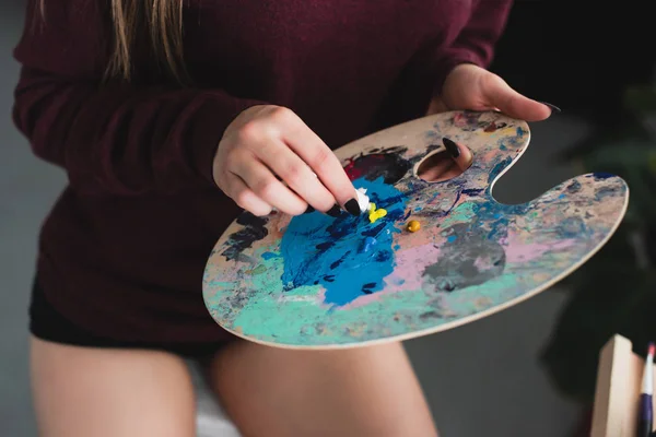 Cropped view of girl in burgundy sweater sitting with palette and painting at home — Stock Photo