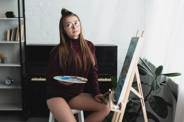 Девушка в бордовом свитере сидит и смотрит в камеру, рисуя дома — стоковое фото