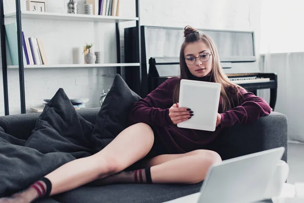 Attraktives Mädchen mit Brille auf dem Sofa liegend und mit digitalem Tablet zu Hause — Stockfoto