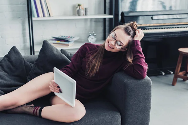 Menina sorridente deitada no sofá e usando tablet digital na sala de estar — Fotografia de Stock