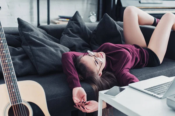 Attractive girl in glasses lying on sofa in living room — Stock Photo