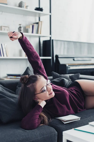 Attractive girl lying on sofa, smiling and raising hand in living room — Stock Photo