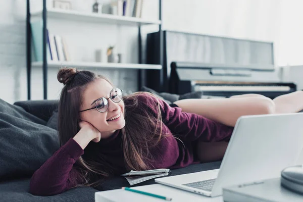 Lächelndes Mädchen auf Sofa liegend und auf Laptop-Bildschirm im Wohnzimmer schauend — Stockfoto