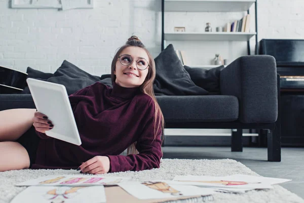 Designer sorridente in occhiali sdraiato sul tappeto e tenendo tablet digitale a casa — Foto stock