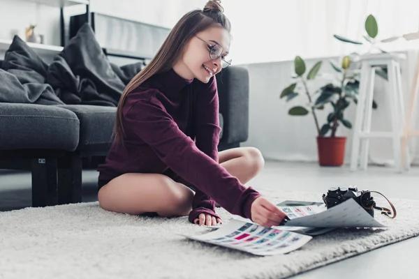 Lächelnder Fotograf sitzt auf Teppich neben Sofa und hält Bilder im Wohnzimmer — Stockfoto