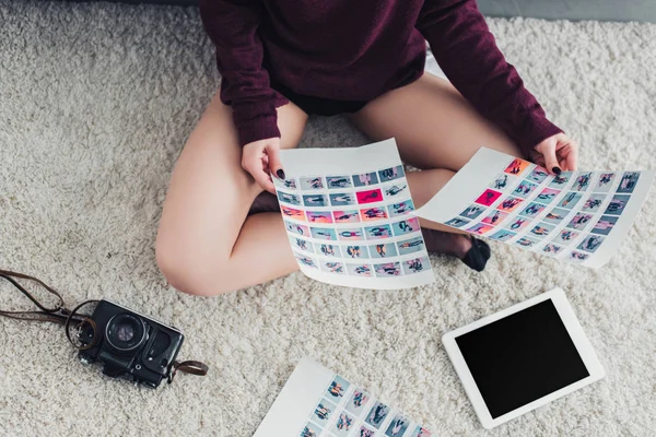 Cropped view of photographer sitting on carpet and holding pictures — Stock Photo