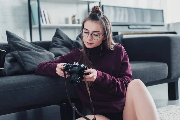 Attraktive Fotografin sitzt auf dem Boden neben Couch und hält Filmkamera im Wohnzimmer — Stockfoto