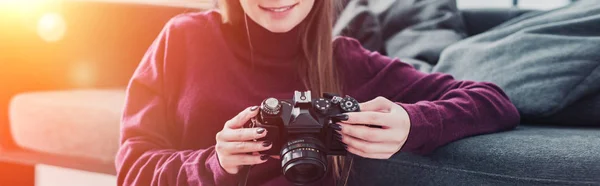 Cropped view of smiling photographer sitting on floor near sofa and holding film camera — Stock Photo