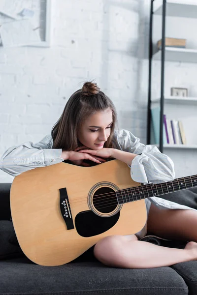 Вдумчивый музыкант сидит на диване и держит акустическую гитару дома — стоковое фото