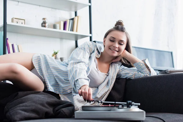 Schöne Musikerin in Hemd und Unterwäsche liegt auf dem Sofa und rührt Vintage Plattenspieler zu Hause an — Stockfoto