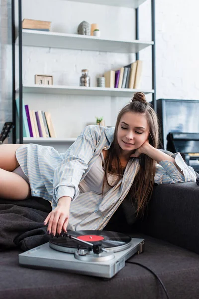 Menina atraente em camisa e roupa interior deitado no sofá e ouvir música em casa — Fotografia de Stock