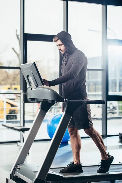Apuesto deportista en sudadera con capucha ejercicio en la cinta de correr en el gimnasio - foto de stock
