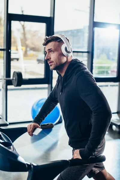 Handsome sportsman in hoodie exercising on treadmill in gym and looking up — Stock Photo