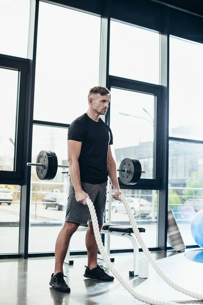Handsome adult sportsman working out with ropes in gym — Stock Photo