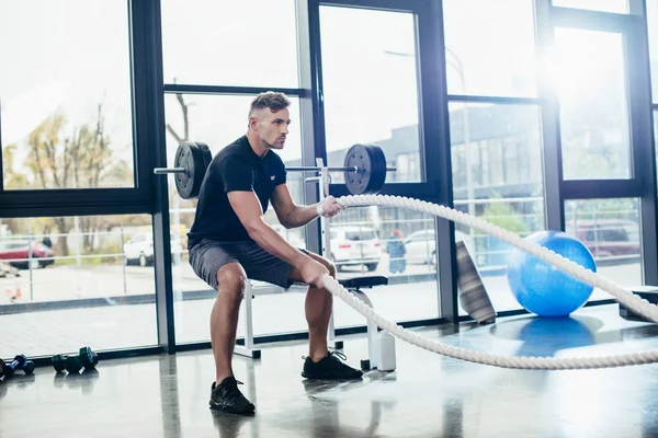 Handsome athletic sportsman working out with ropes in gym — Stock Photo