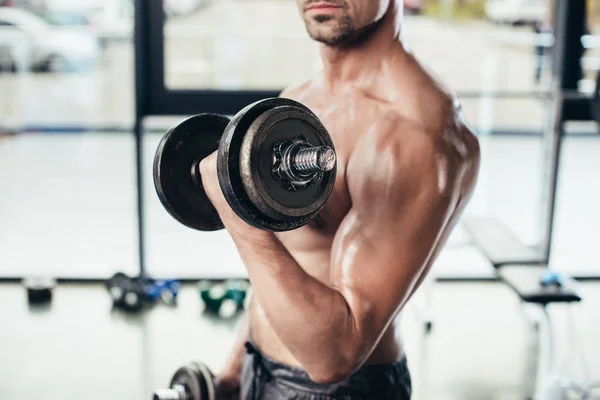 Imagen recortada de un deportista sudoroso sin camisa entrenando con pesas en el gimnasio - foto de stock
