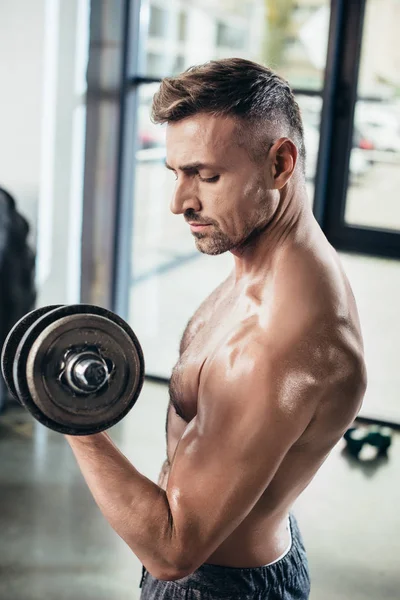 Side view of handsome shirtless sportsman training with dumbbell in gym — Stock Photo
