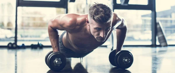 Handsome shirtless sportsman training with dumbbells and doing plank in gym — Stock Photo