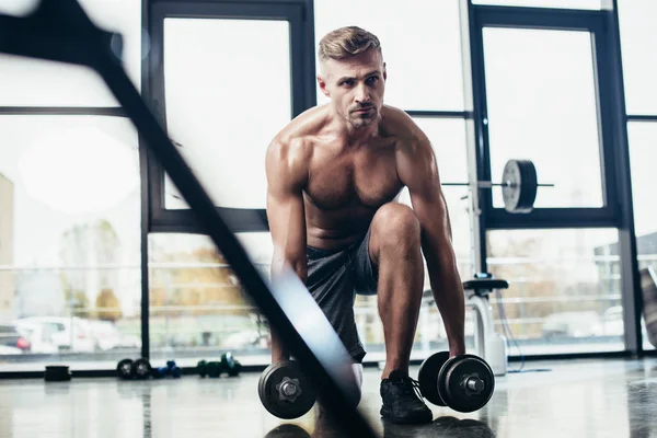 Selective focus of handsome shirtless sportsman training with dumbbells in gym — Stock Photo