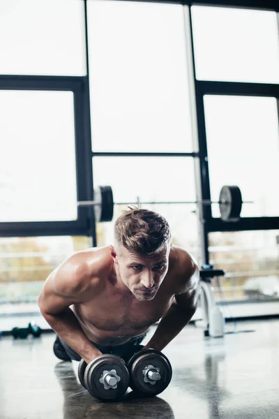 Handsome shirtless sportsman doing plank on dumbbells in gym — Stock Photo