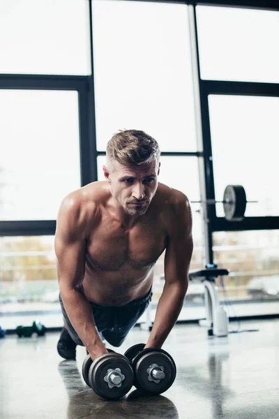 Handsome muscular sportsman doing plank on dumbbells in gym — Stock Photo