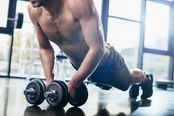 Cropped image of shirtless sportsman doing plank on dumbbells in gym — Stock Photo