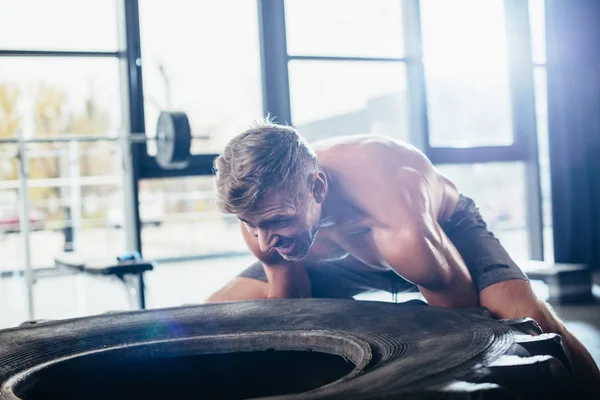 Schöner hemdloser Sportler, der schwere Reifen in der Turnhalle hebt — Stockfoto