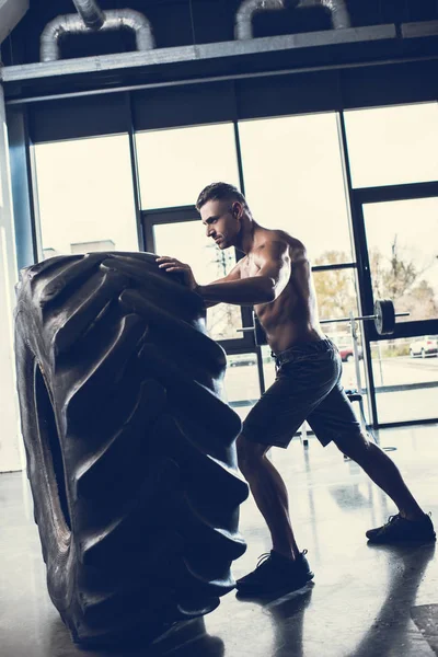 Vista lateral del guapo deportista sin camisa levantando neumáticos en el gimnasio - foto de stock