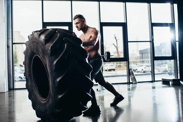 Side view of handsome shirtless sportsman working out and lifting tire in gym — Stock Photo