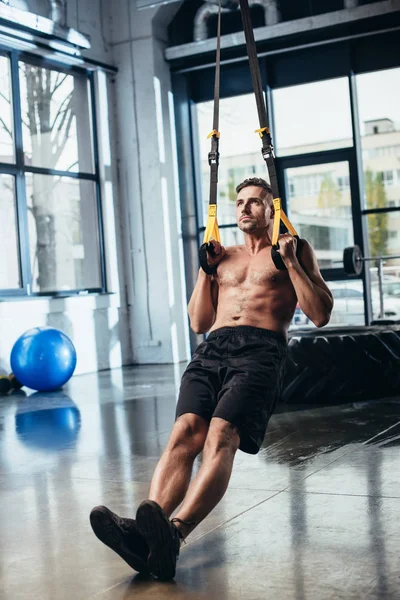 Handsome shirtless sportsman training with suspension straps in gym — Stock Photo