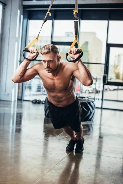 Handsome shirtless sportsman exercising with resistance bands in gym — Stock Photo