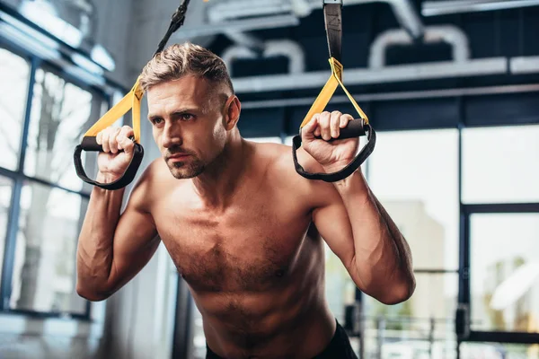Handsome shirtless sportsman working out with resistance bands in gym — Stock Photo