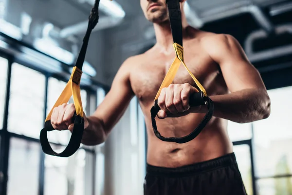 Cropped image of shirtless sportsman training with resistance bands in gym — Stock Photo